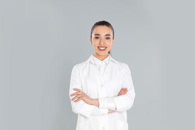 Happy young woman in lab coat on light grey background