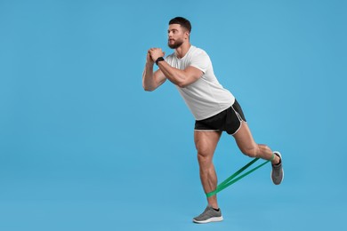 Young man exercising with elastic resistance band on light blue background. Space for text