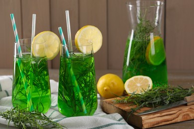 Photo of Jug and glasses of refreshing tarragon drink with lemon slices on table