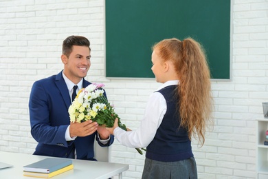Photo of Schoolgirl congratulating her pedagogue with bouquet in classroom. Teacher's day