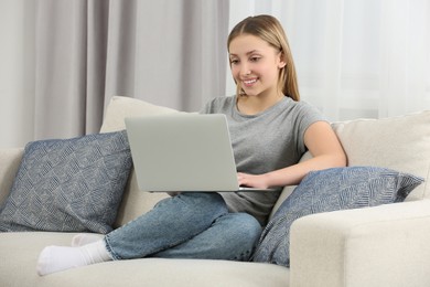 Teenage girl using laptop on sofa at home