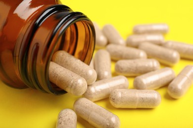 Photo of Gelatin capsules and bottle on yellow background, closeup