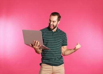 Emotional young man with laptop celebrating victory on color background