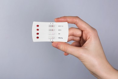 Woman holding disposable multi-infection express test on light grey background, closeup