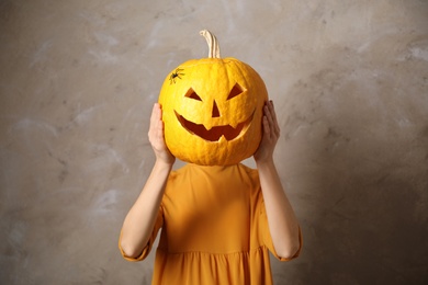 Photo of Woman with pumpkin head against beige background. Jack lantern - traditional Halloween decor