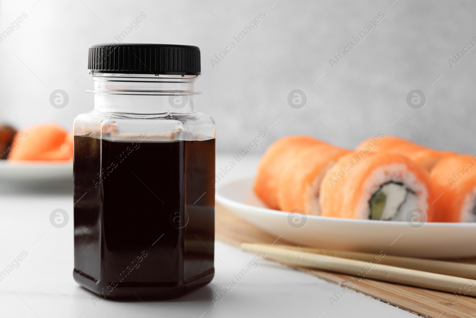 Photo of Bottle of tasty soy sauce, chopsticks and sushi rolls with salmon on white table, closeup. Space for text