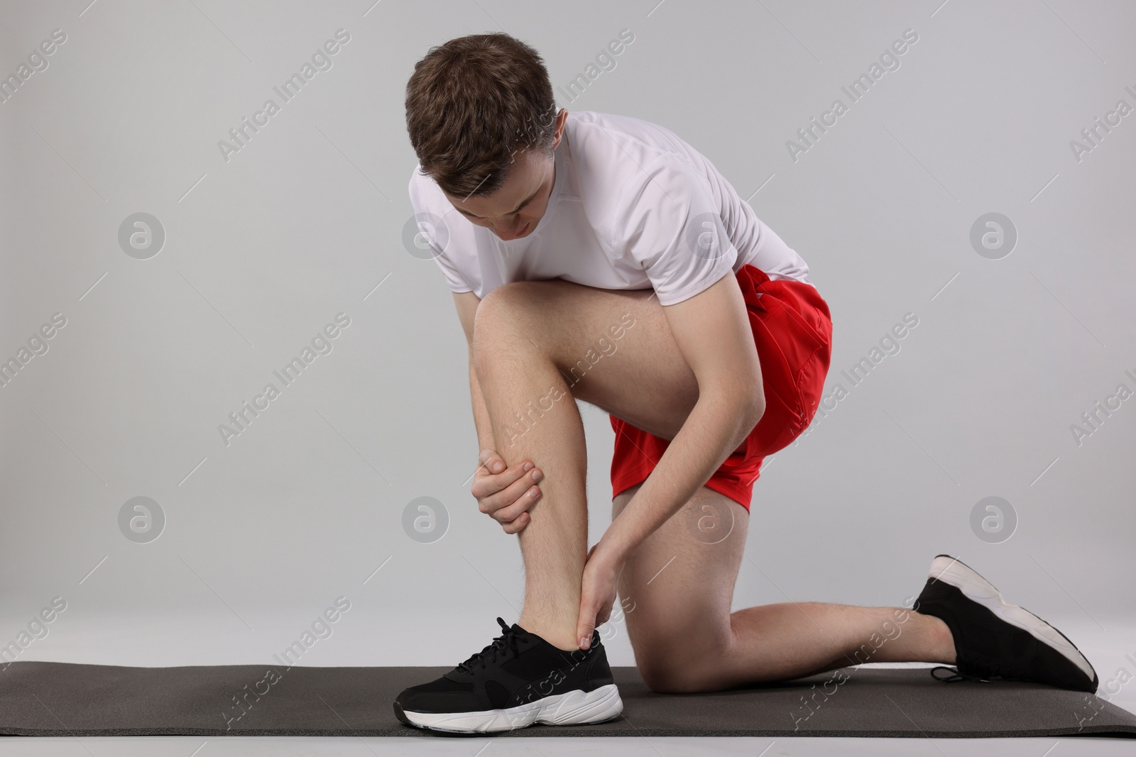 Photo of Man suffering from leg pain on mat against grey background