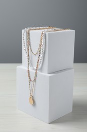 Stylish presentation of necklaces on podiums on white wooden table
