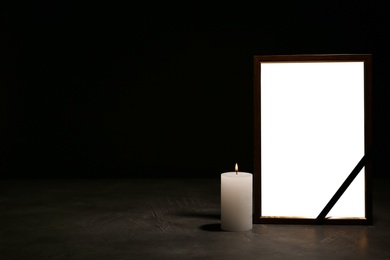 Photo of Empty frame with black ribbon and candle on table. Funeral symbol