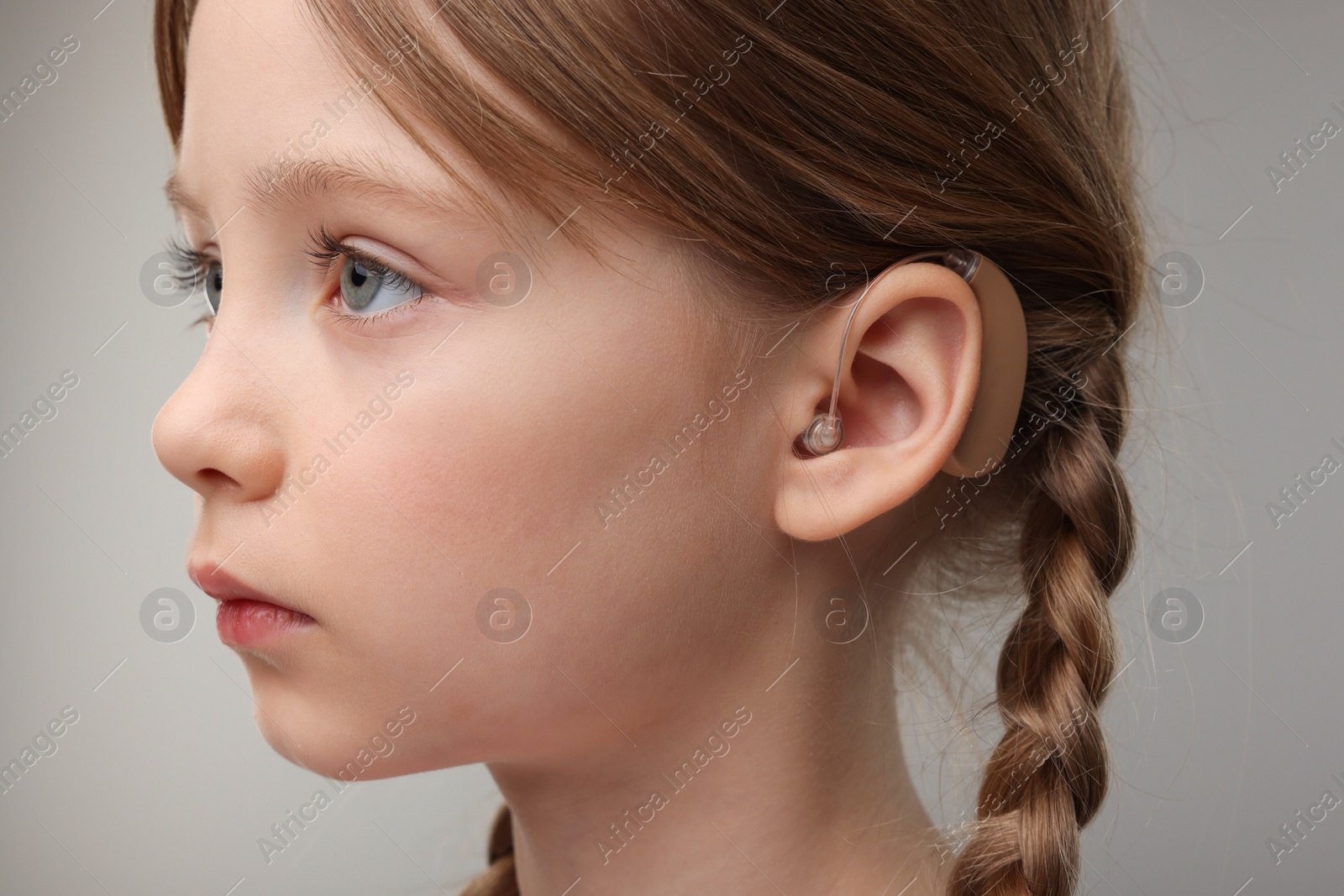 Photo of Little girl with hearing aid on grey background, closeup