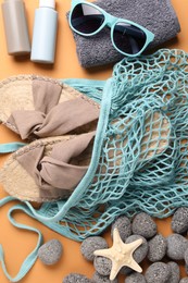 String bag and different beach accessories on pale orange background, flat lay