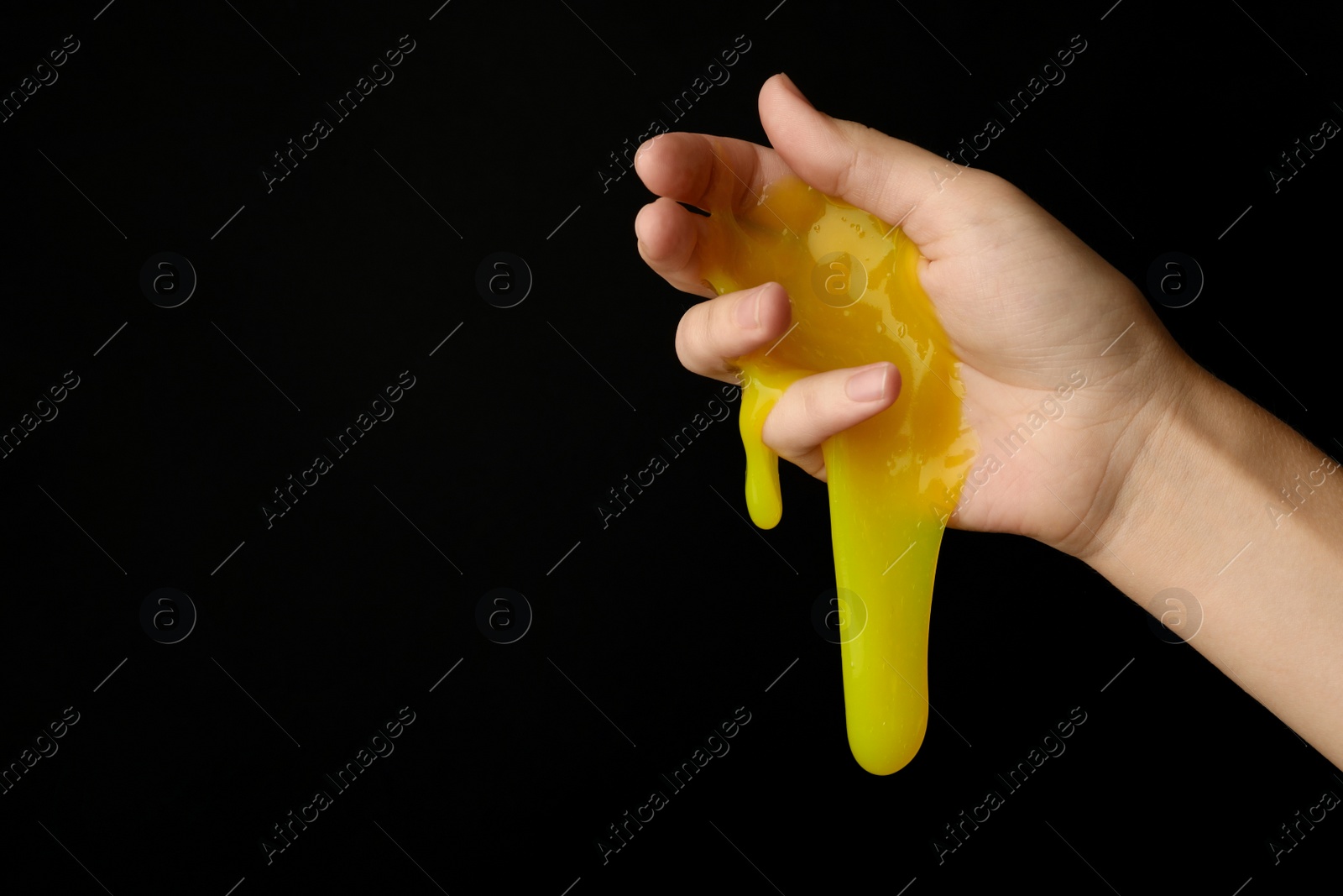 Photo of Woman playing with yellow slime on black background, closeup. Antistress toy