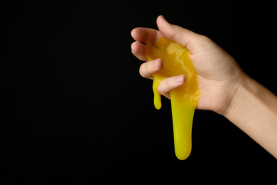 Photo of Woman playing with yellow slime on black background, closeup. Antistress toy