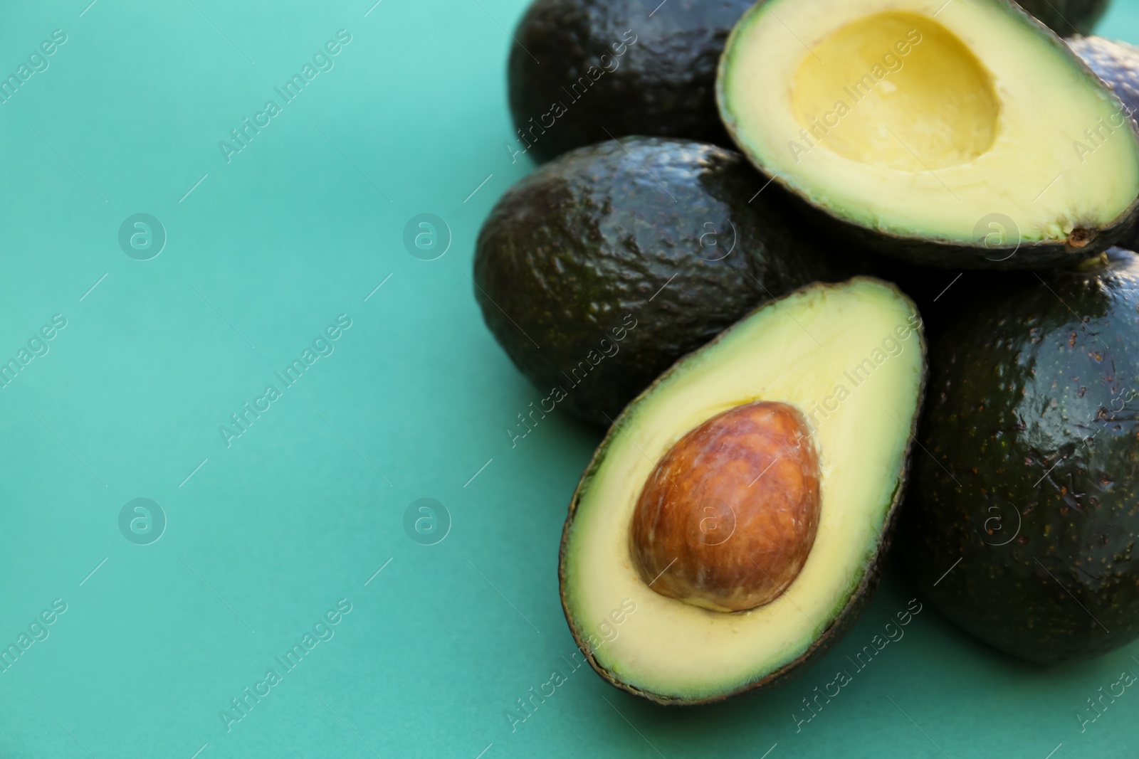 Photo of Tasty whole and cut avocados on turquoise background. Space for text