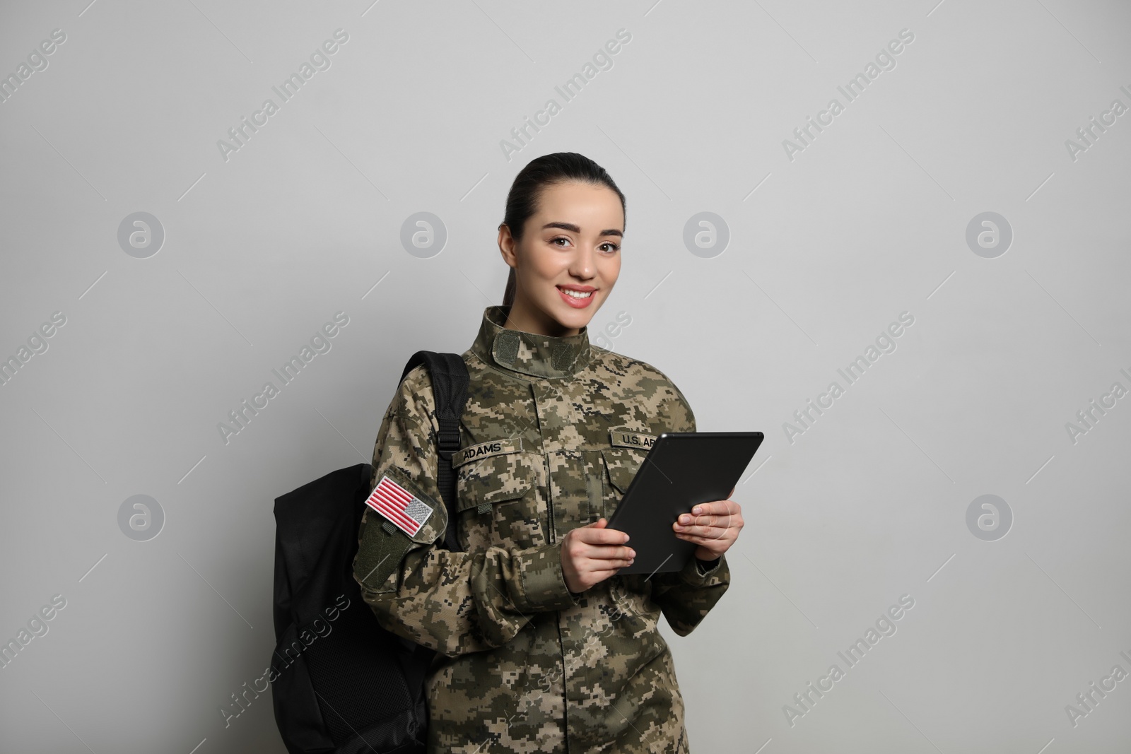 Photo of Female soldier with tablet and backpack on light grey background. Military education