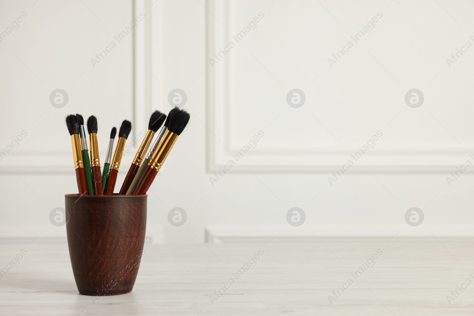 Photo of Different paintbrushes in holder on white wooden table. Space for text