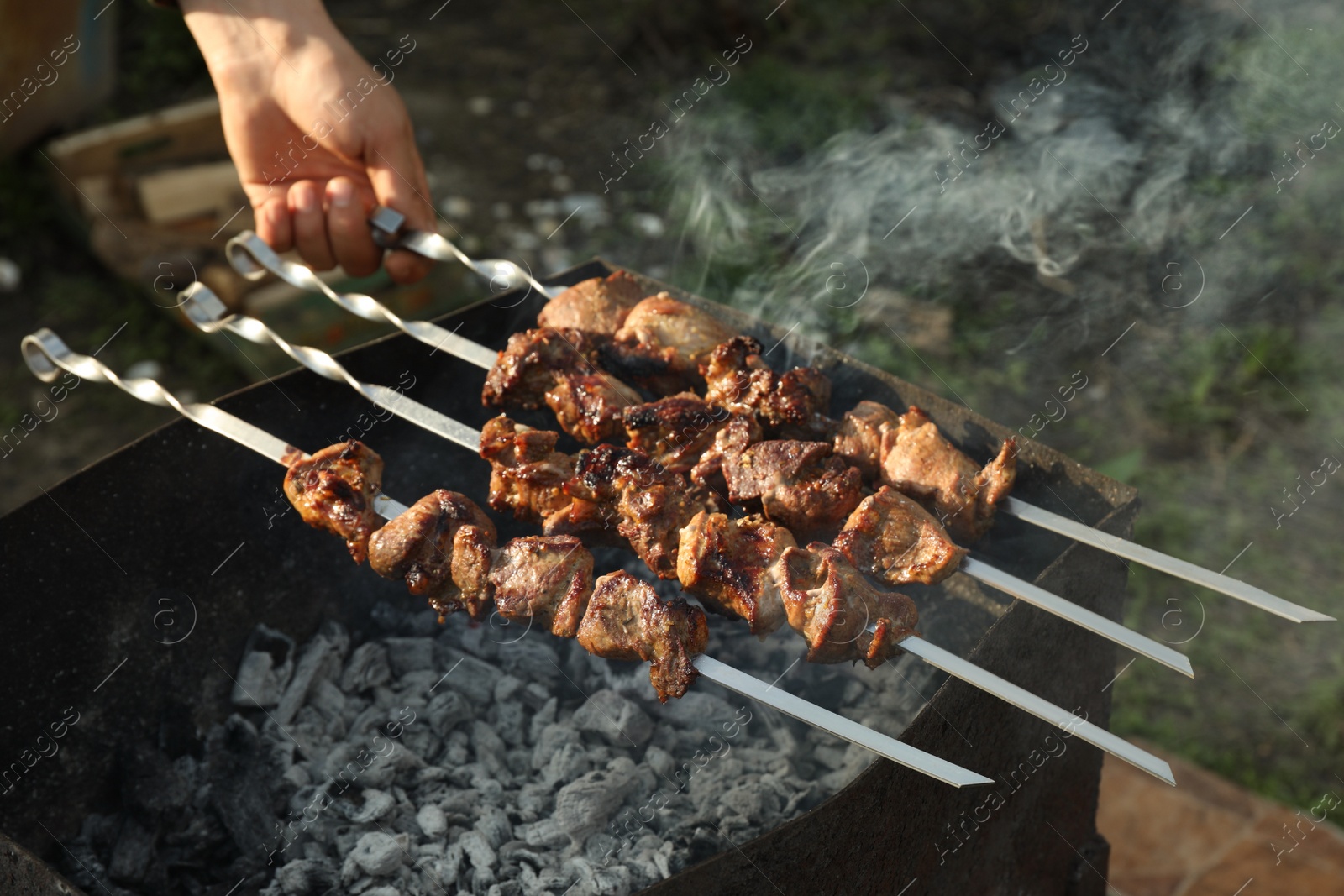 Photo of Man cooking delicious meat on brazier outdoors, closeup