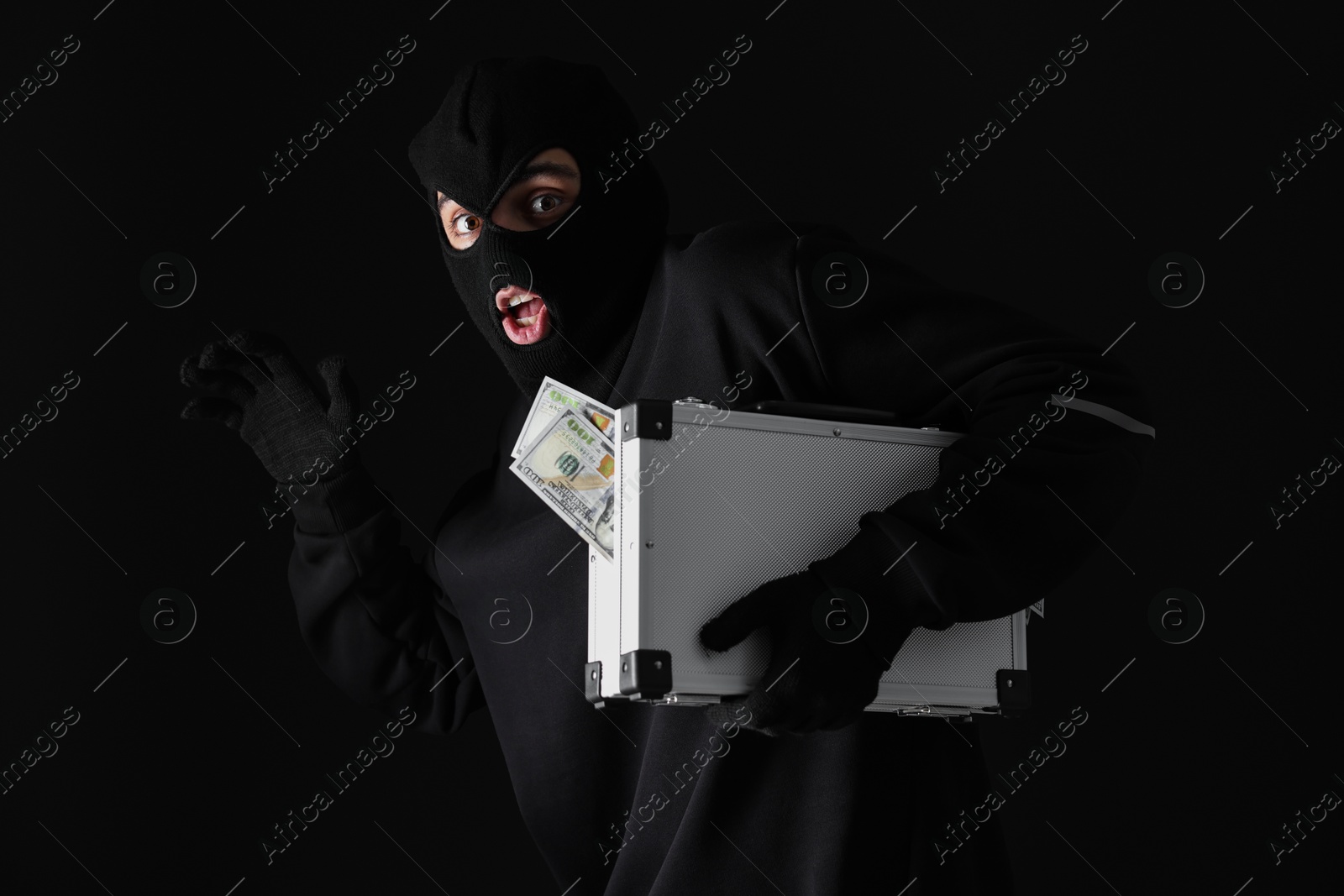 Photo of Emotional thief in balaclava with briefcase of money on black background