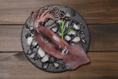 Photo of Fresh raw squid with ice and rosemary on wooden table, top view