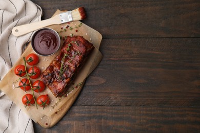 Photo of Tasty roasted pork ribs served with sauce and tomatoes on wooden table, top view. Space for text