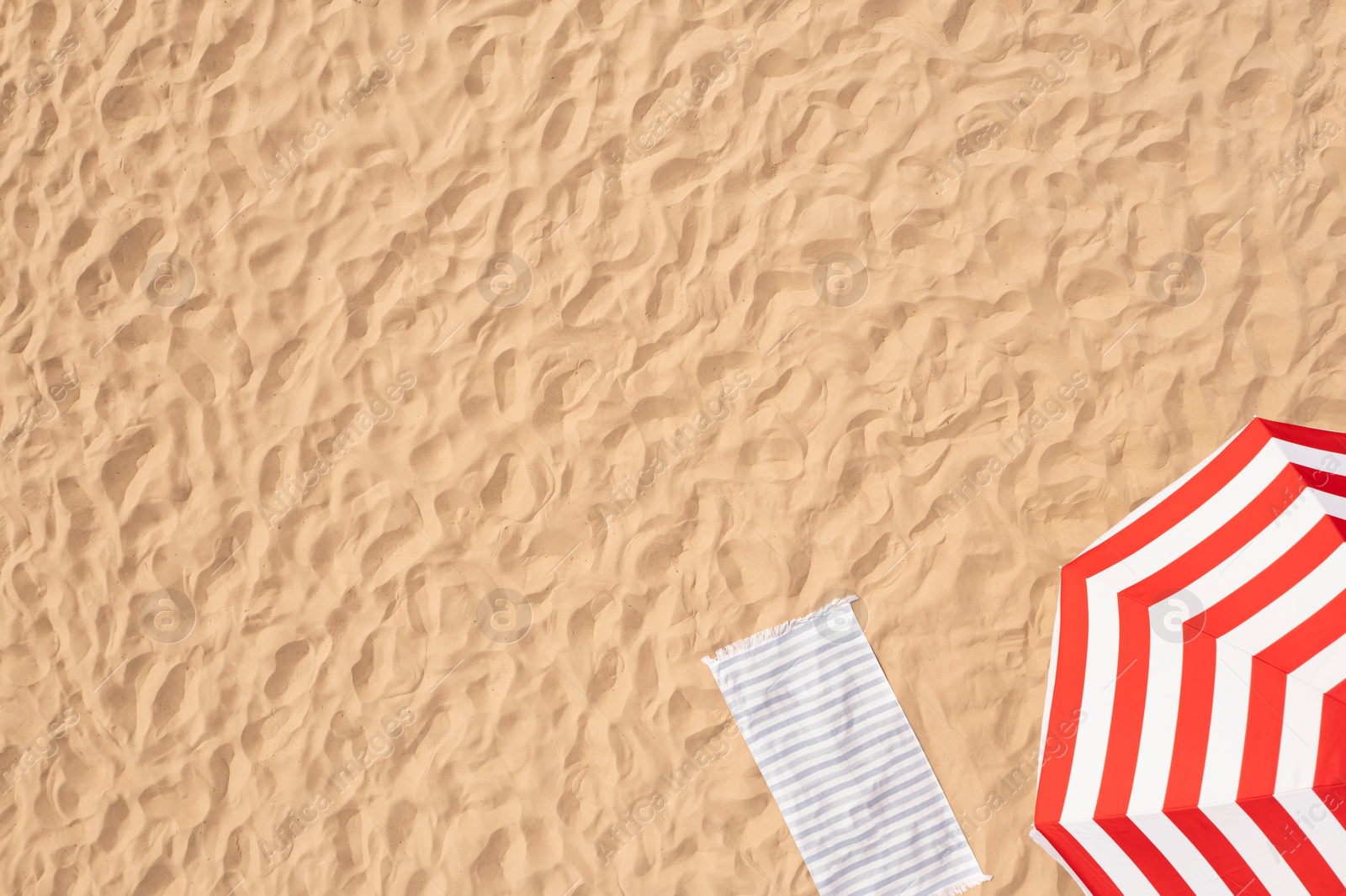 Image of Striped beach umbrella near towel on sand, aerial view. Space for text