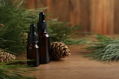 Photo of Pine essential oil, cones and branches on wooden table. Space for text