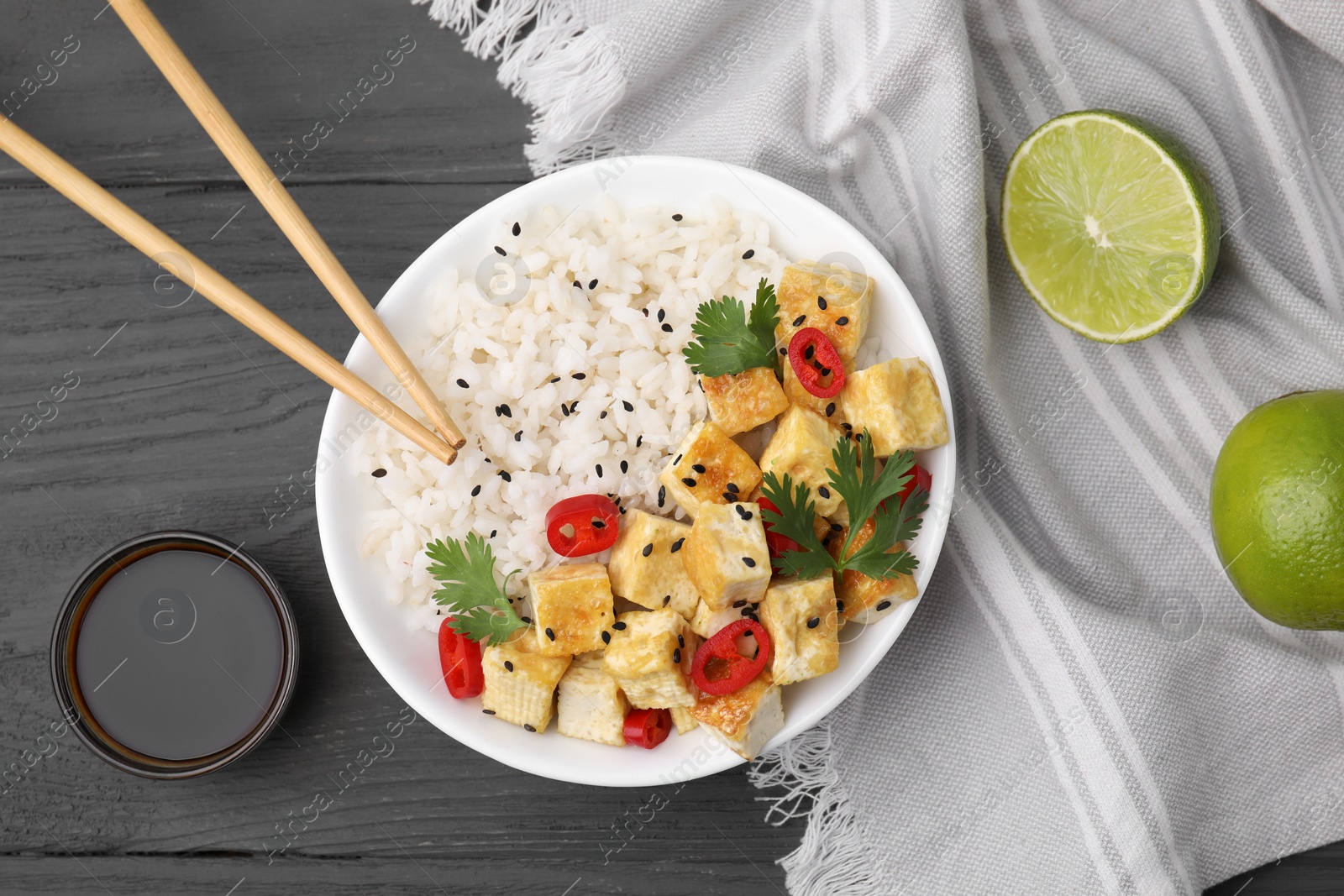 Photo of Delicious rice with fried tofu, chili pepper and parsley served on grey wooden table, flat lay