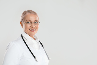 Portrait of mature doctor with stethoscope on light grey background. Space for text