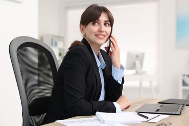 Smiling secretary talking by smartphone at table in office