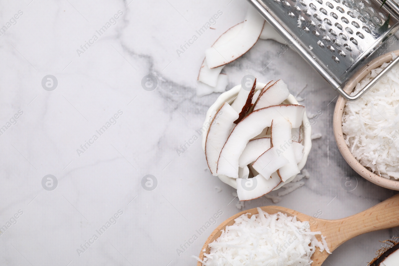 Photo of Coconut flakes, pieces, spoon and grater on white marble table, flat lay. Space for text