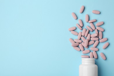 Photo of Vitamin pills and bottle on light blue background, top view. Space for text