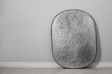 Studio reflector near grey wall in room, space for text. Professional photographer's equipment