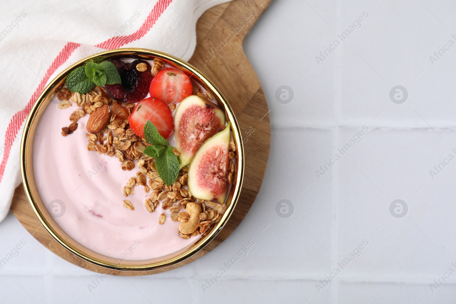 Photo of Bowl with yogurt, fruits and granola on white tiled table, top view. Space for text