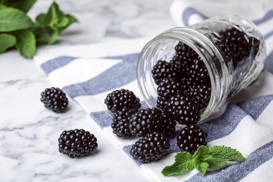 Photo of Glass jar with tasty ripe blackberries on marble table