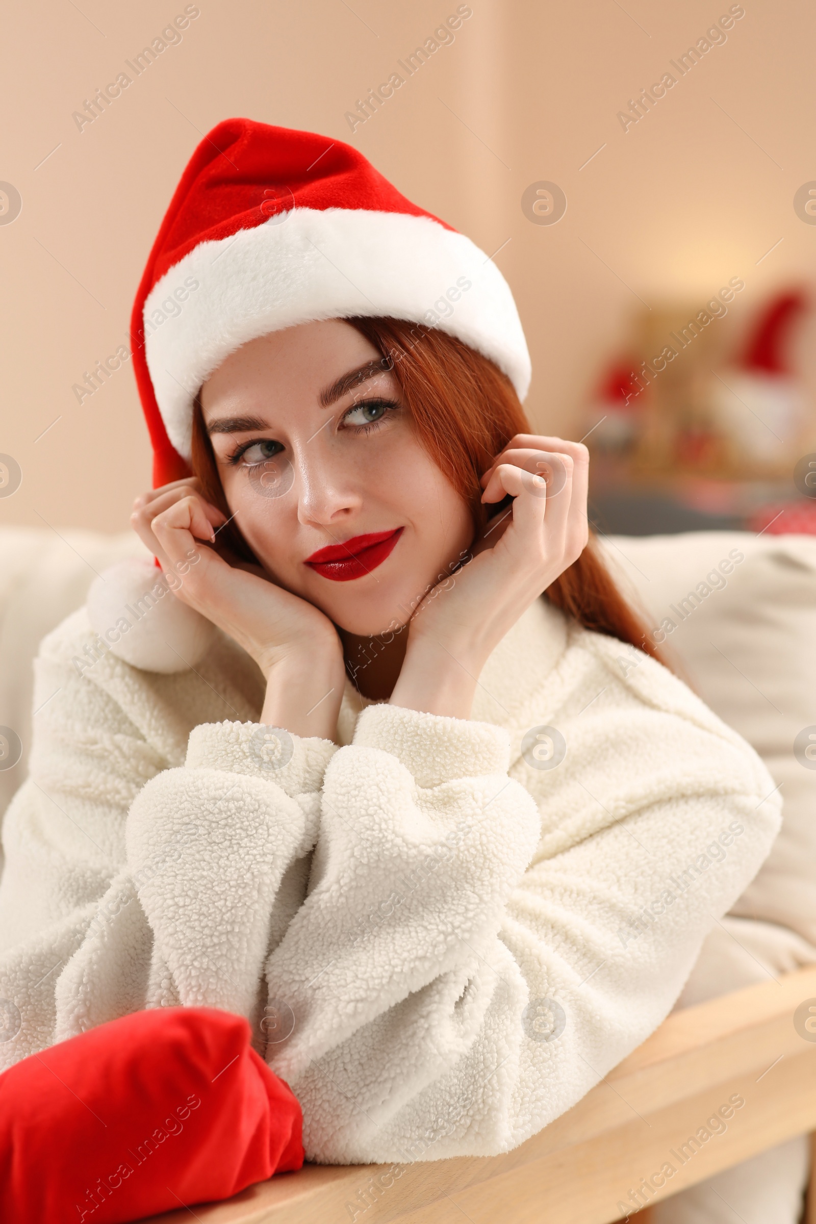Photo of Beautiful young woman in Santa hat on sofa at home. Celebrating Christmas