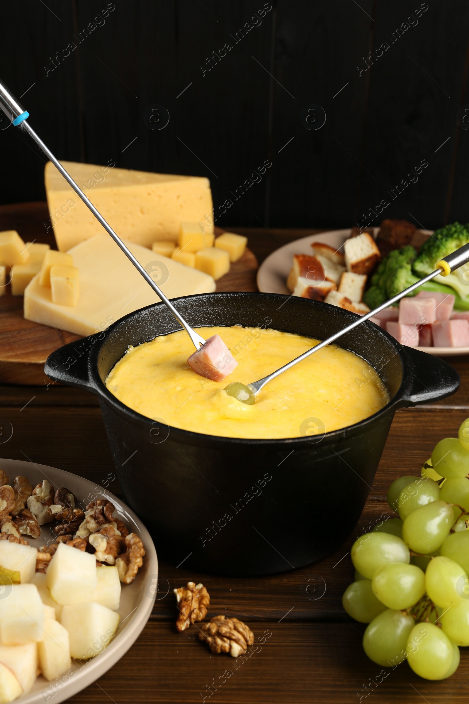 Photo of Fondue pot with melted cheese, forks and different products on wooden table