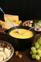 Photo of Fondue pot with melted cheese, forks and different products on wooden table