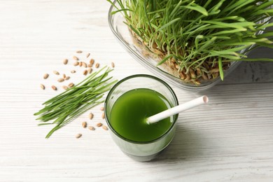 Wheat grass drink in glass, seeds and fresh green sprouts on white wooden table, flat lay