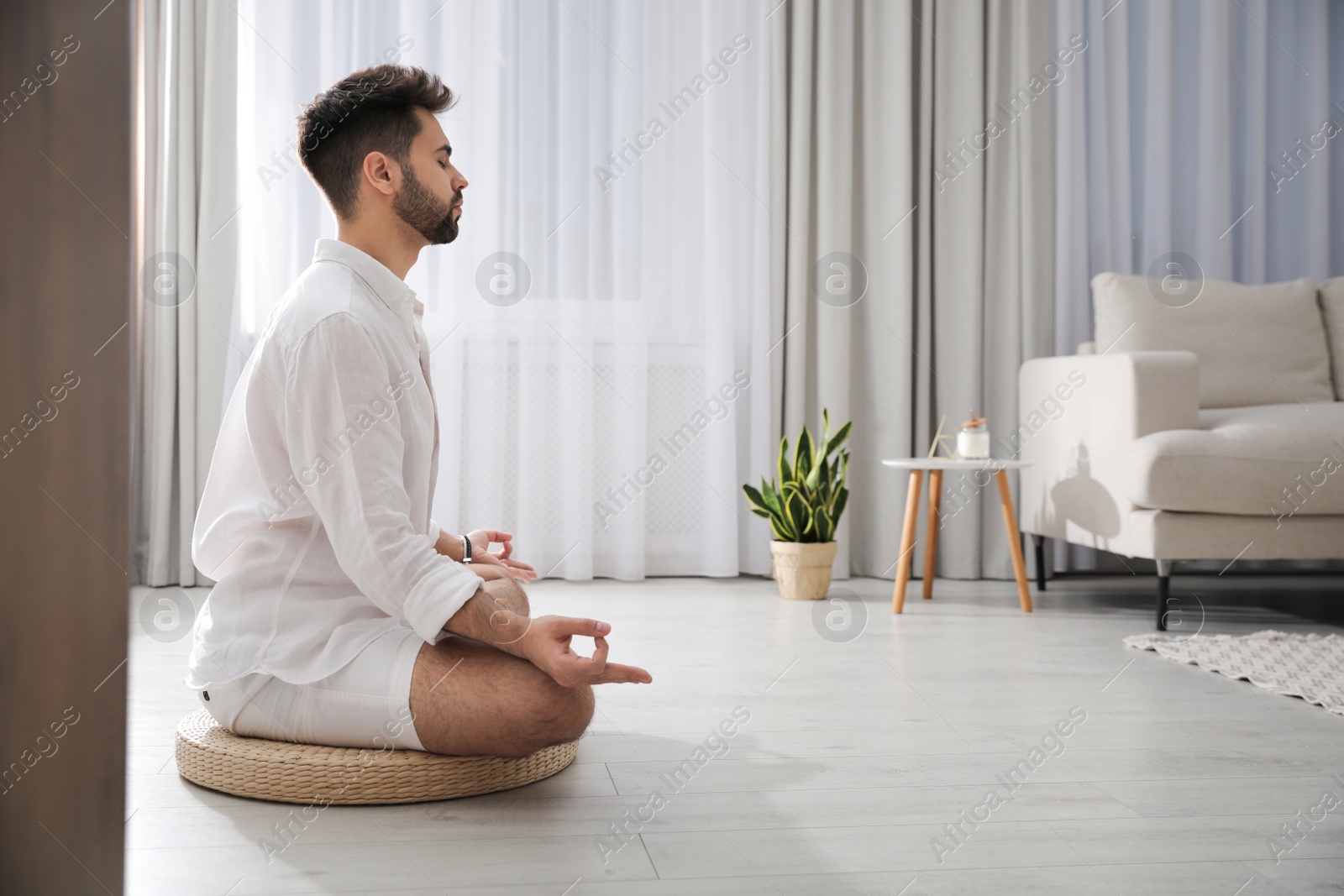 Photo of Young man meditating on straw cushion at home, space for text