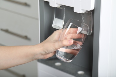 Woman filling glass with water cooler, closeup. Refreshing drink