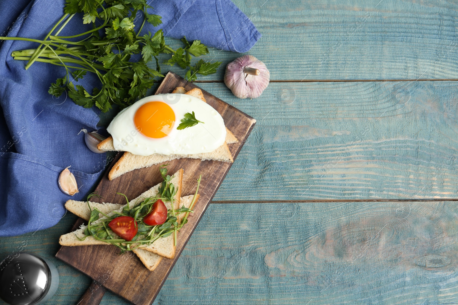 Photo of Tasty fried egg served with bread, tomato and sprouts on blue wooden table, flat lay. Space for text