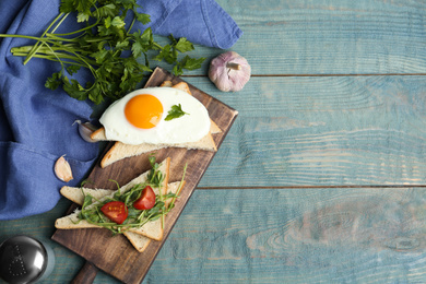 Photo of Tasty fried egg served with bread, tomato and sprouts on blue wooden table, flat lay. Space for text