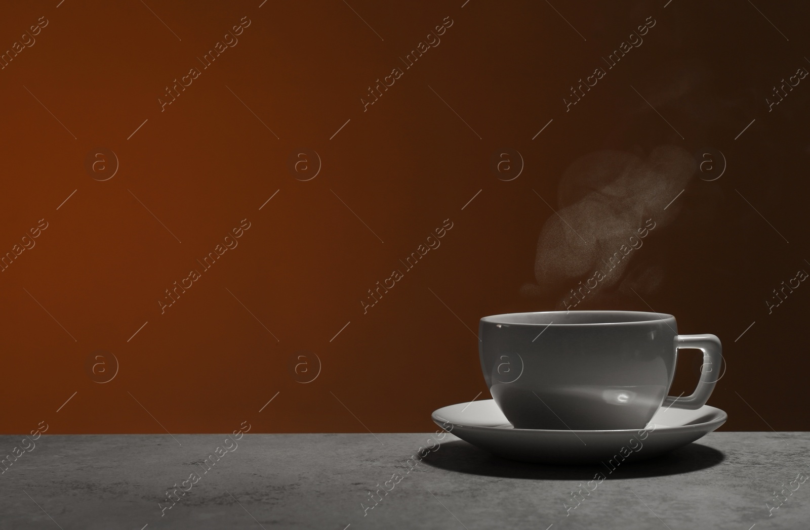 Photo of Ceramic cup of hot fresh tea on stone table against brown background, space for text