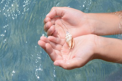 Kid holding seashell in hands above water outdoors, closeup