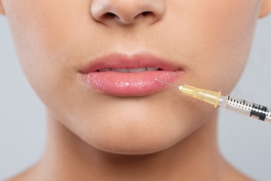 Young woman getting lips injection on grey background, closeup. Cosmetic surgery