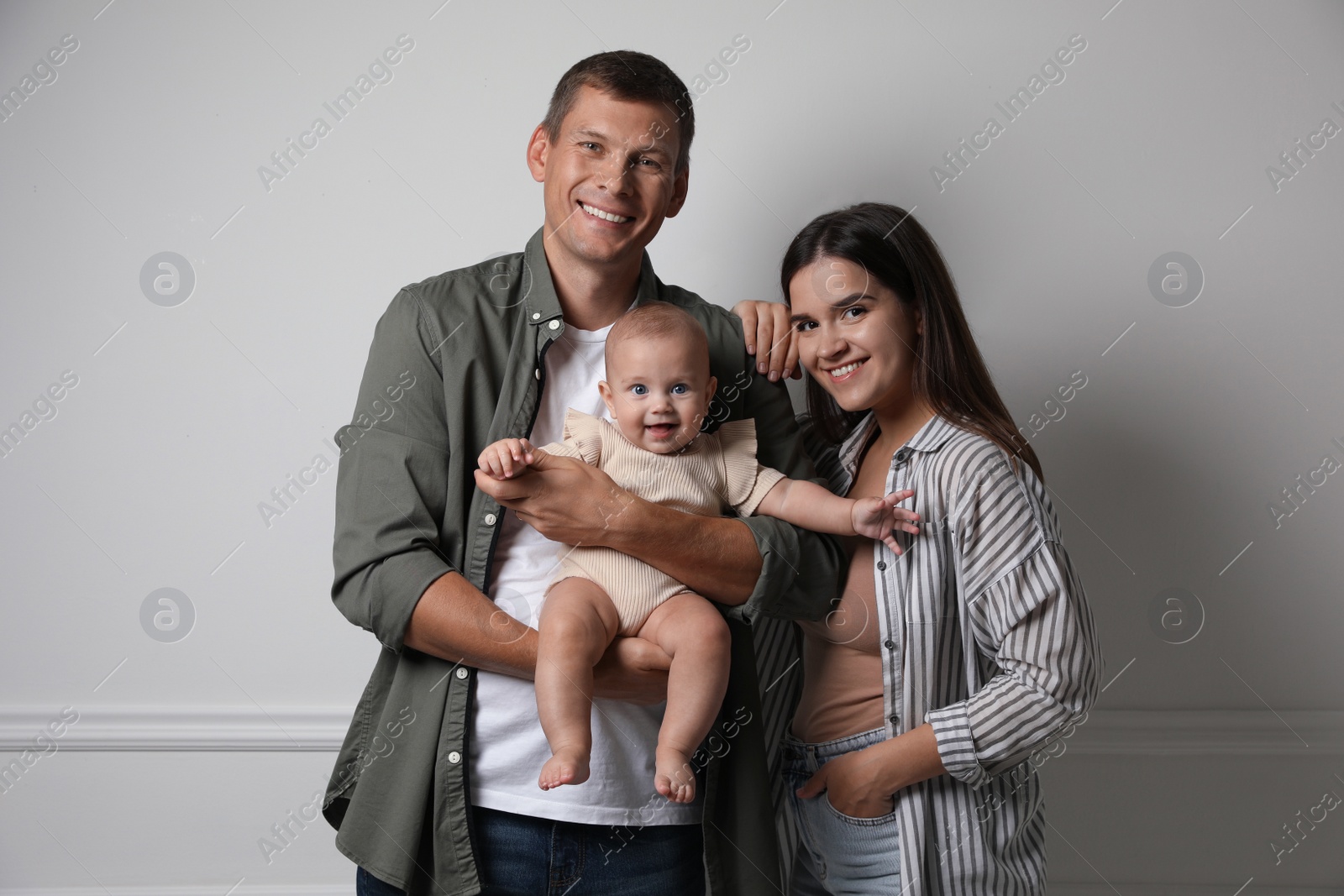 Photo of Happy family. Couple with their cute baby near light wall