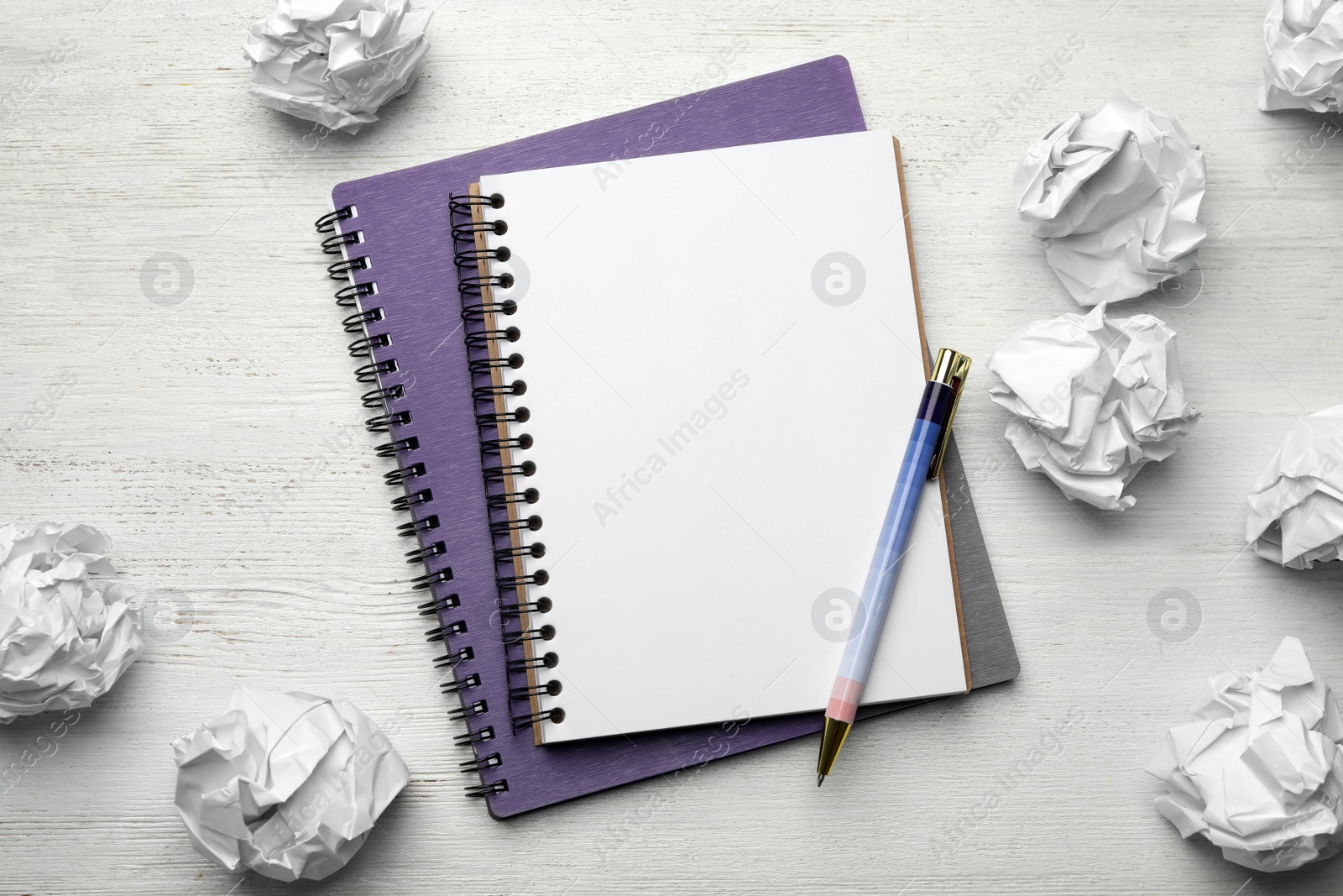Photo of Notebooks with pen and crumpled paper balls on white wooden table, flat lay. Space for text