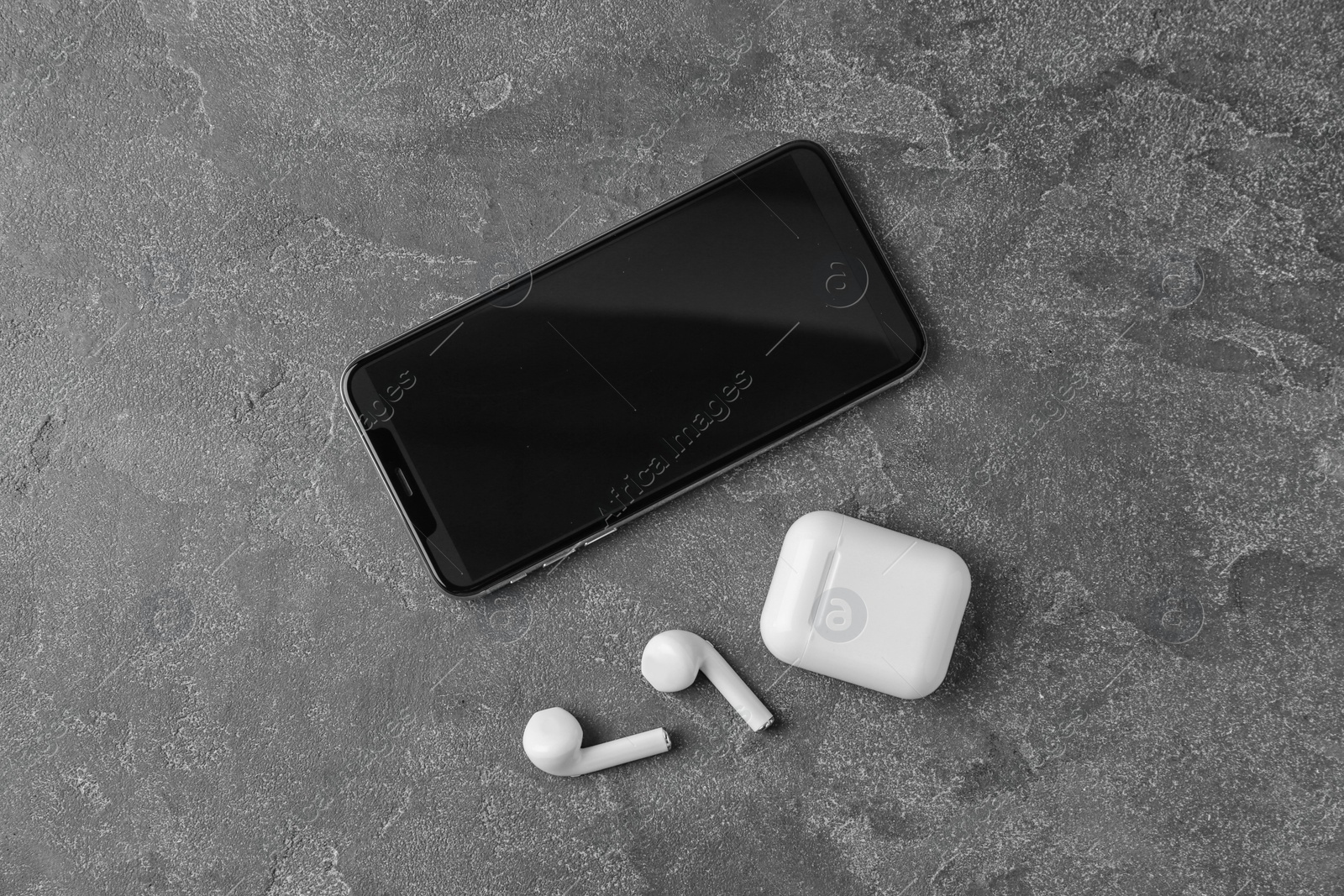 Photo of Wireless earphones, mobile phone and charging case on grey stone table, flat lay. Space for text