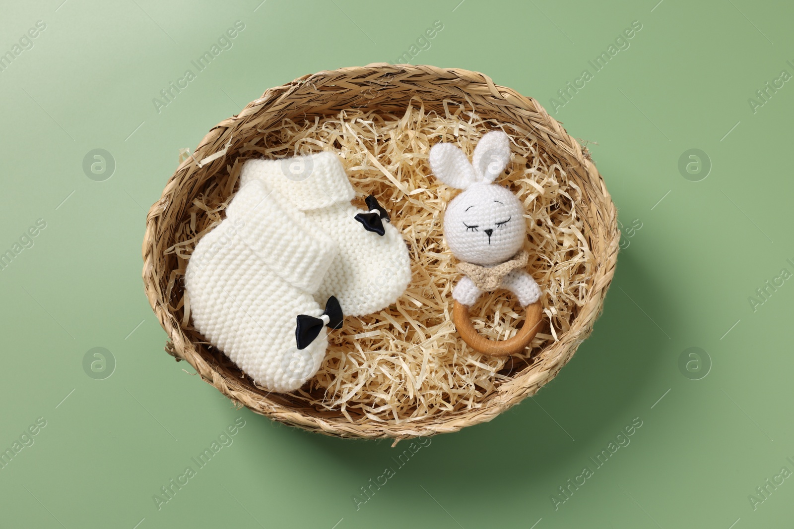 Photo of Different baby accessories in wicker box on green background, top view