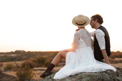 Photo of Happy newlyweds sitting on rock at sunset